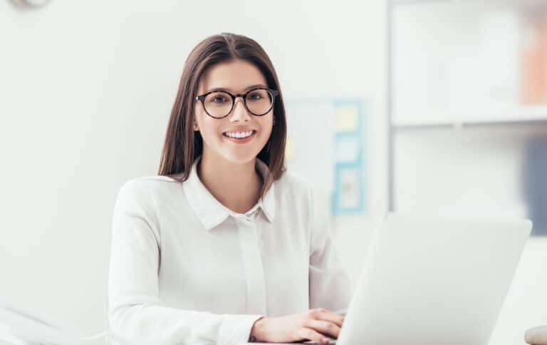 Frau sitzt vor Laptop und lacht in die Kamera. Bewerben Sie sich als Mitarbeiter / Assistenz (m/w/d) Marketing & Onlinevertrieb