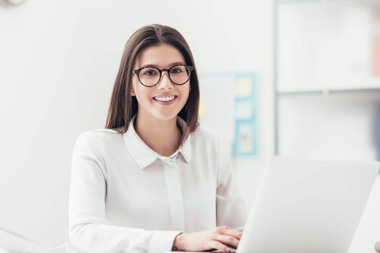 Frau sitzt vor Laptop und lacht in die Kamera. Bewerben Sie sich als Mitarbeiter / Assistenz (m/w/d) Marketing & Onlinevertrieb