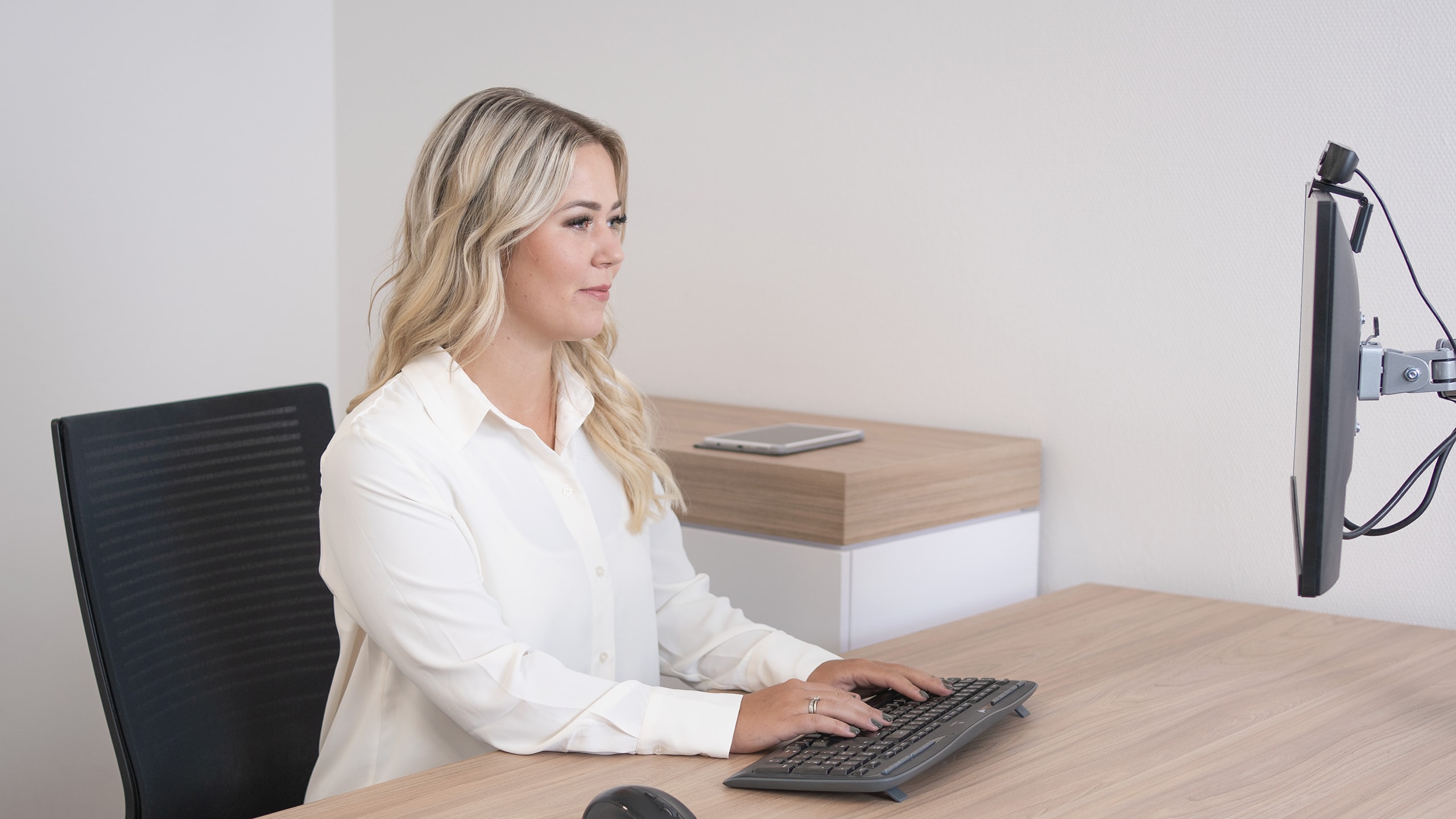 Dame sitzt am Schreibtisch und schaut auf einen Monitor.