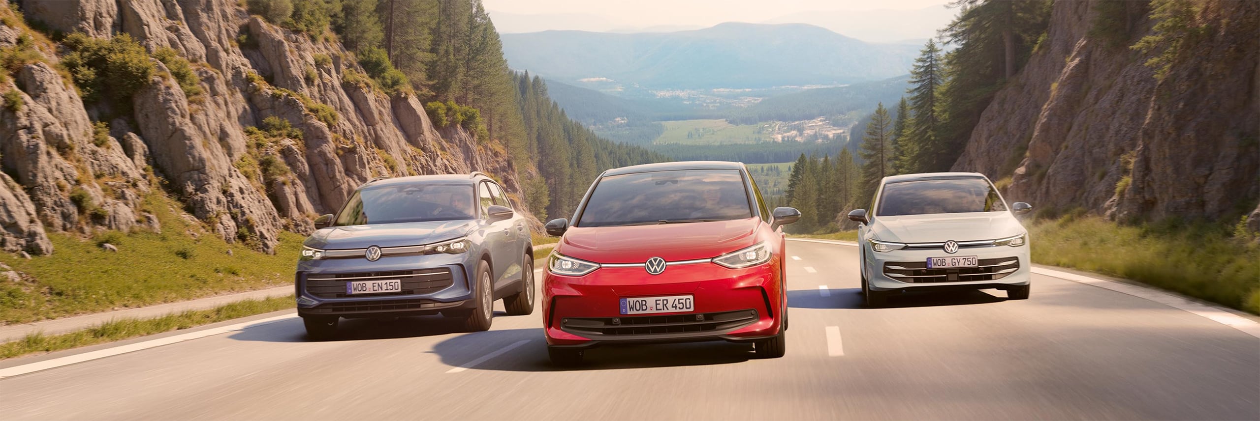 Drei Volkswagen Autos fahren nebeneinander auf einer Bergstrecke.